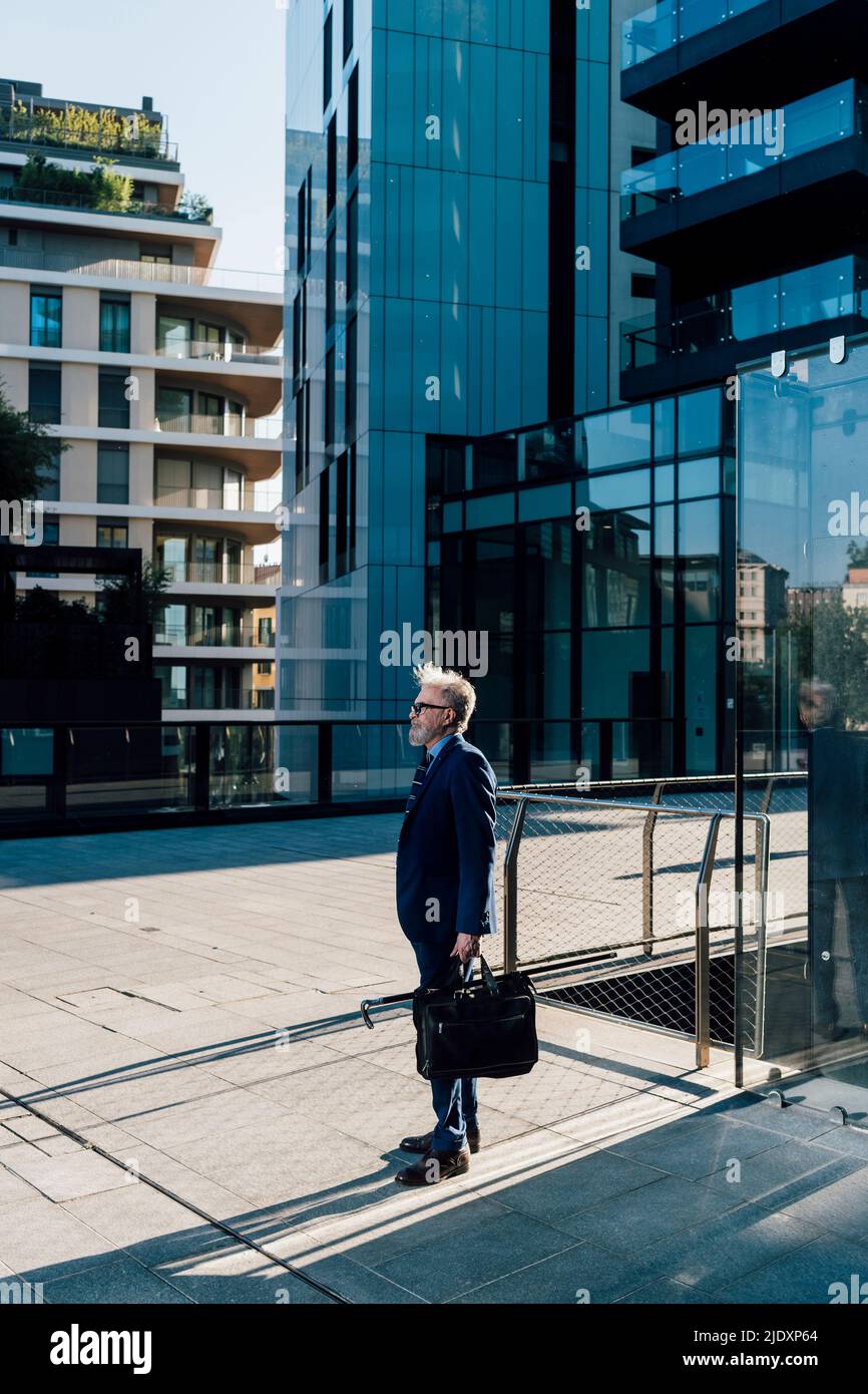 Senior businessman standing with briefcase outside office building exterior Stock Photo