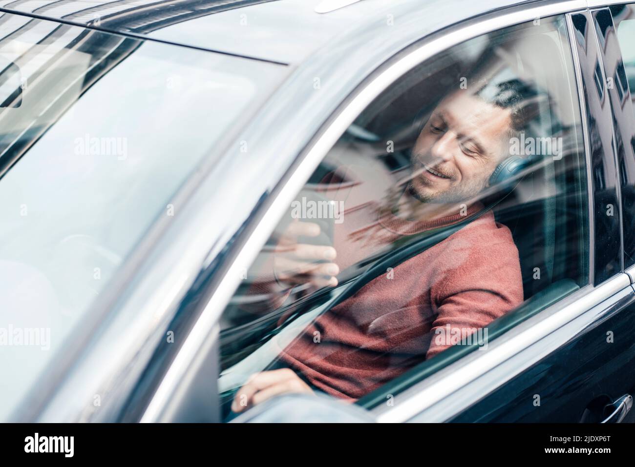 Smiling man using smart phone sitting in car Stock Photo