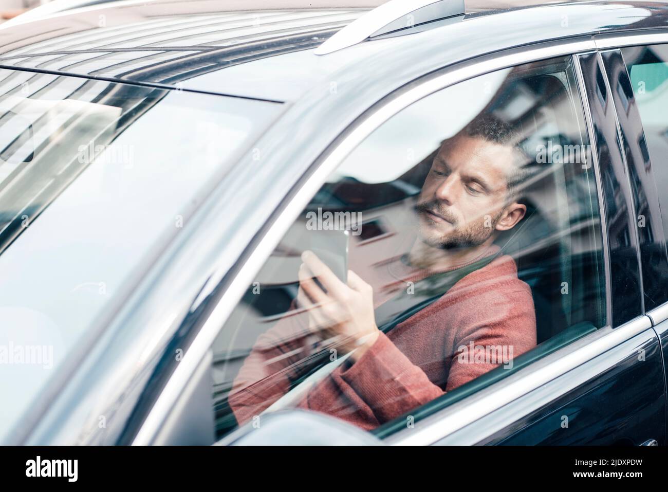 Man using smart phone sitting in car seen through window Stock Photo