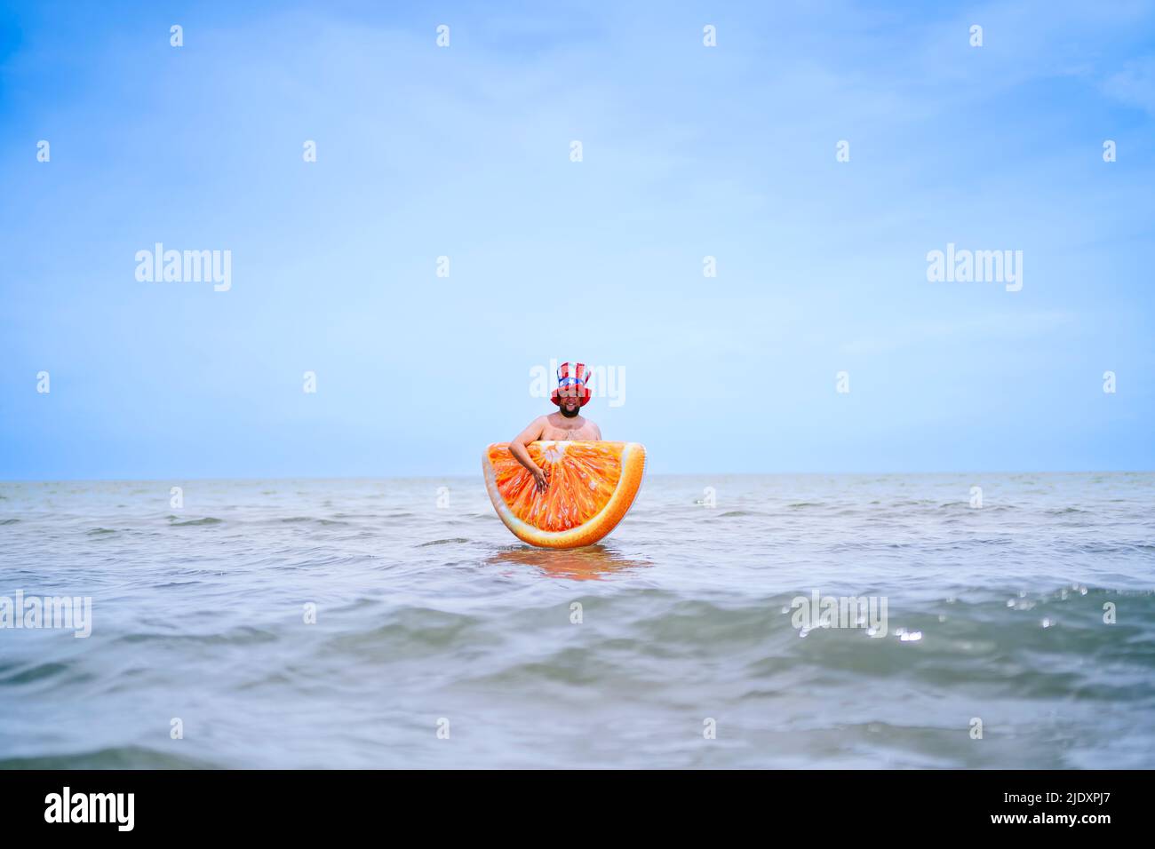 Man carrying inflatable orange slice standing in sea Stock Photo