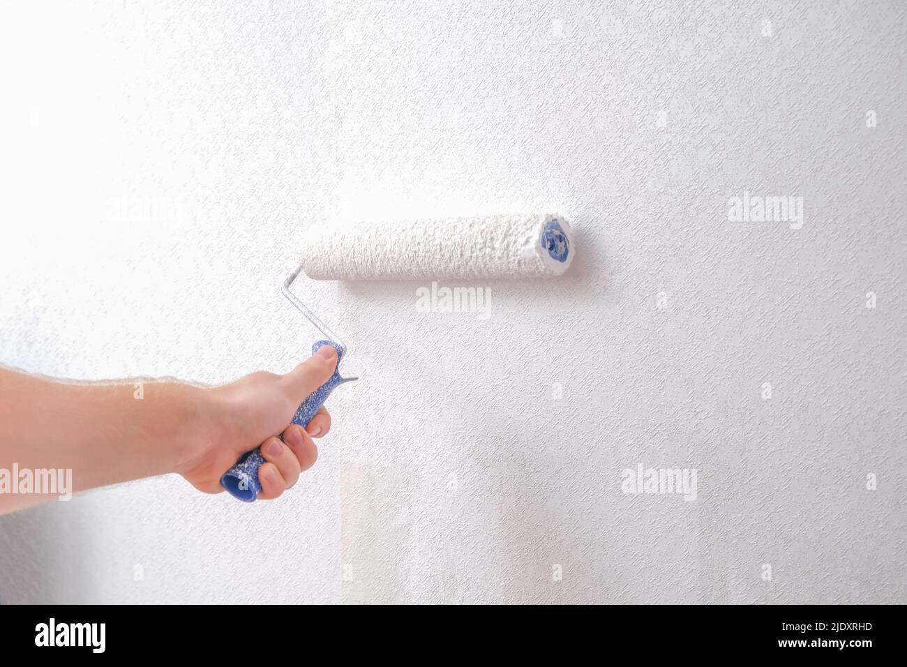 A man is painting vinyl wallpaper with a velour roller for painting
