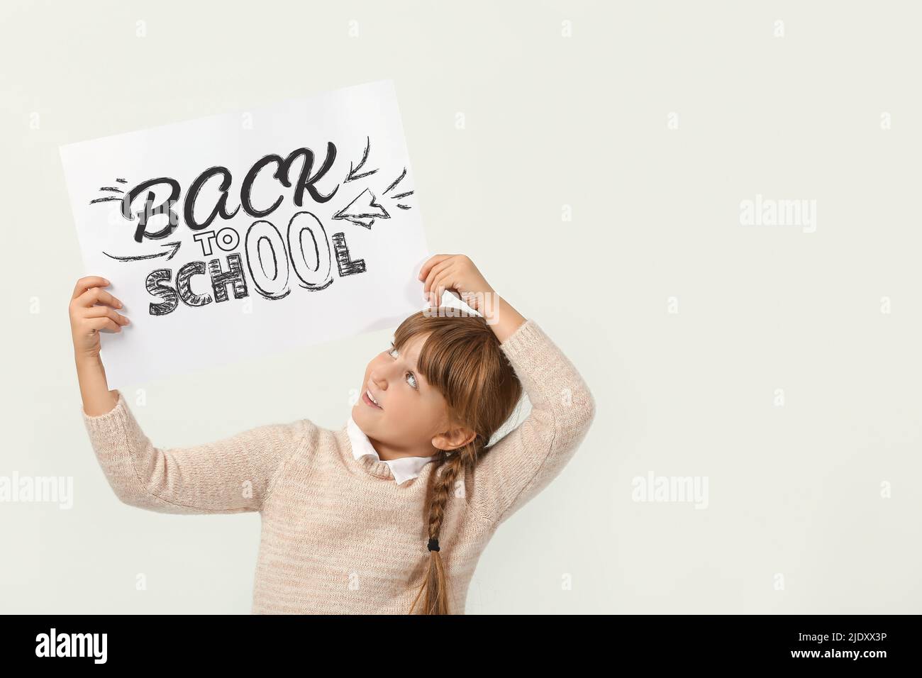 Cute little girl holding poster with text BACK TO SCHOOL on light ...