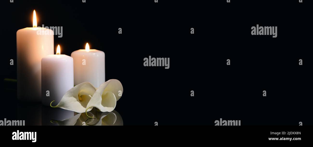 Burning candles and flowers on black background with space for text