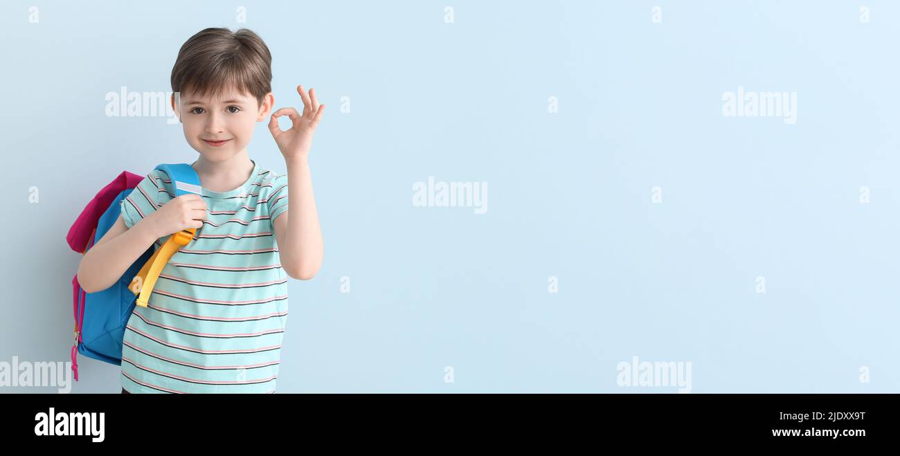 Cute little schoolboy showing OK on light blue background with space ...