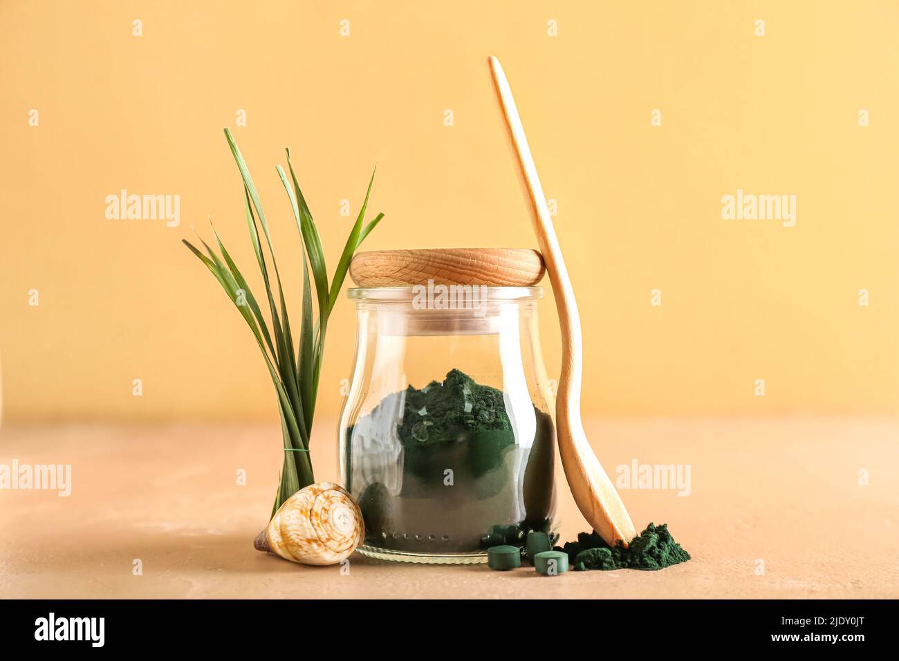 Glass jar of spirulina powder, spoon, pills, seashell and leaves on ...