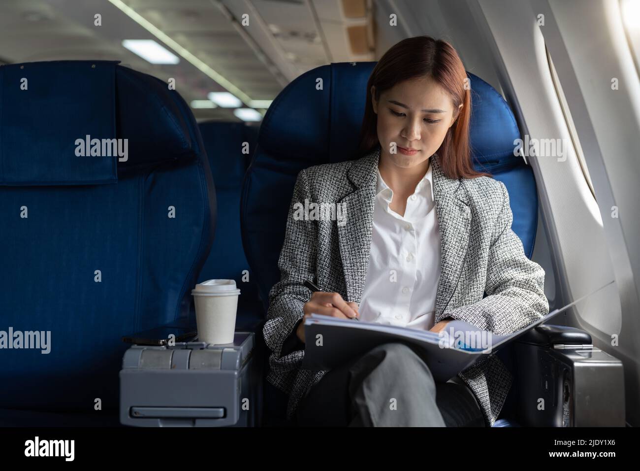 Asian female entrepreneur working on paperwork finance report sitting near window in an airplane Stock Photo