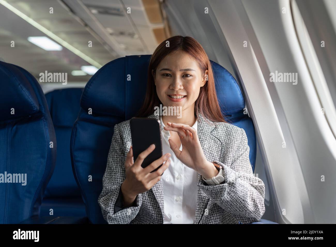Portrait attractive asian woman use of mobile phone on airplane, looking at camera. Stock Photo