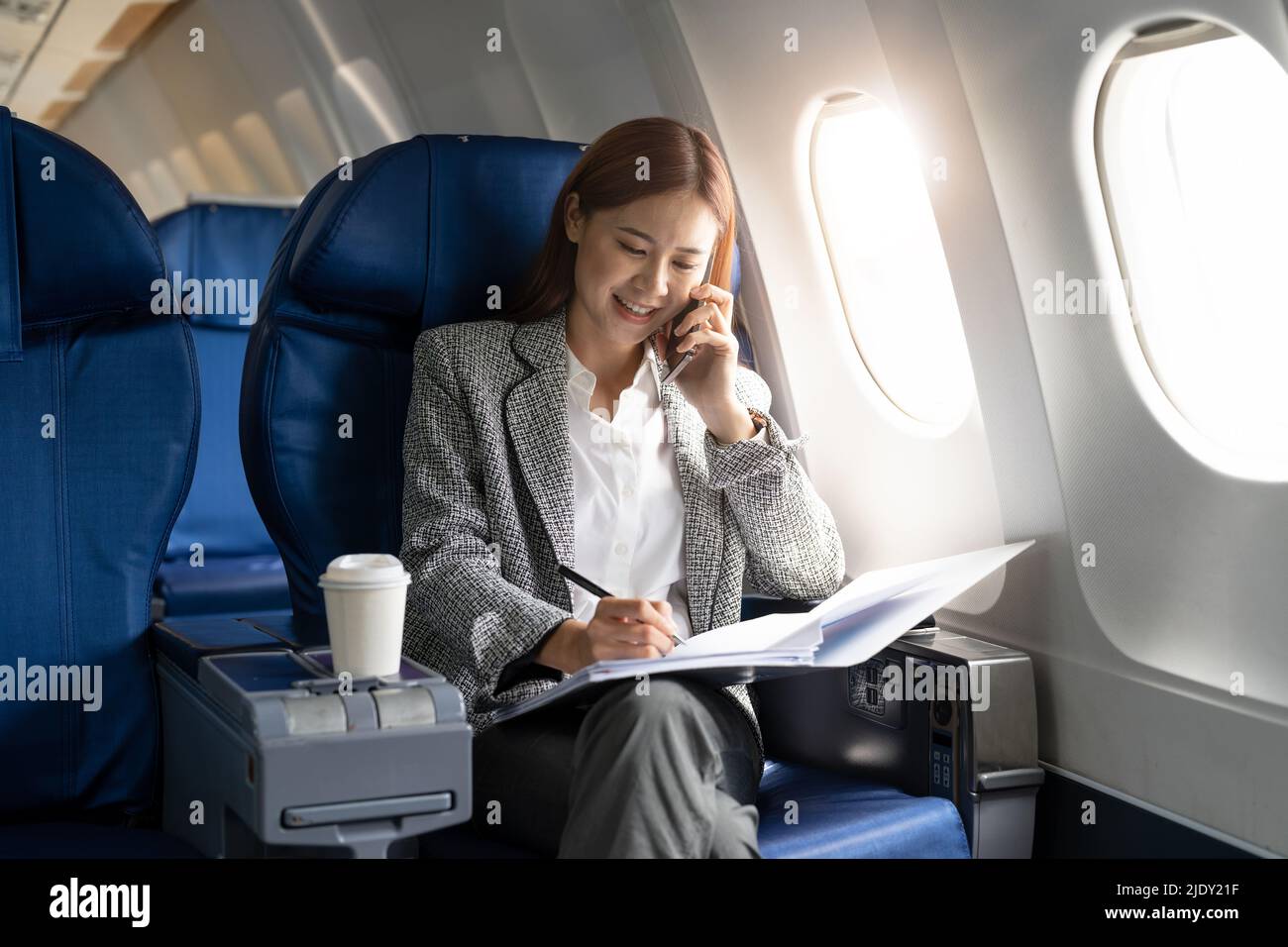 Business young asian woman talking on phone during working for paperwork financial report on airplane, flight in plane Stock Photo