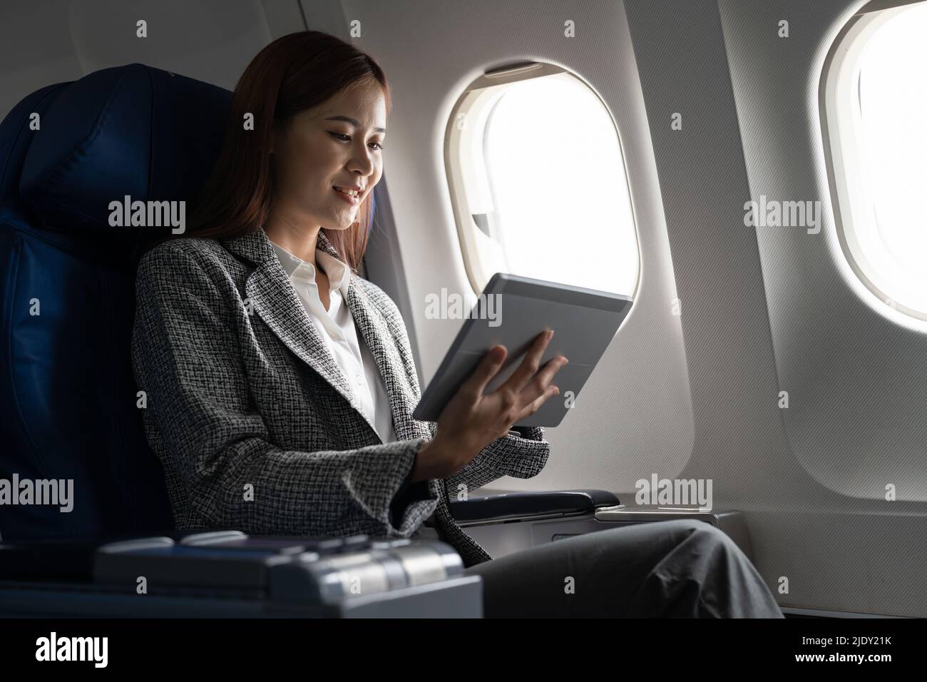 Travel and technology. Young asian woman in plane using digital tablet while sitting in airplane seat Stock Photo