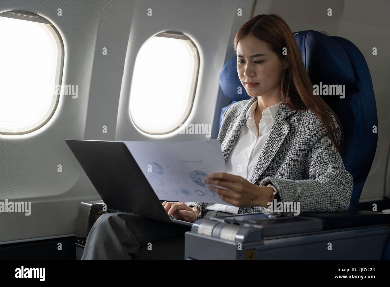 Asian young woman using laptop with financial report sitting near windows at first class on airplane during flight, Traveling and Business concept Stock Photo
