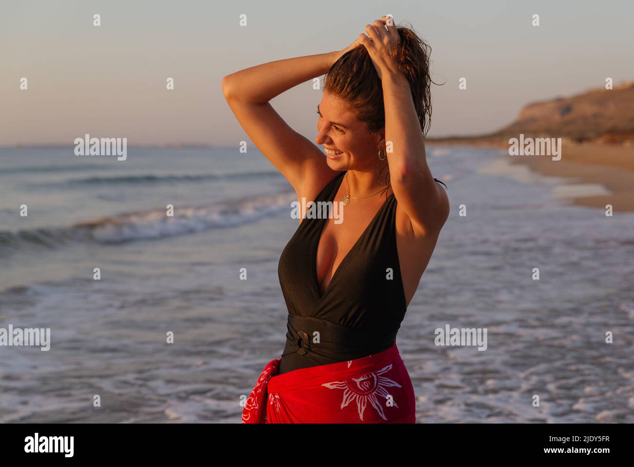 Happy, young woman in black swimsuit has fun on the seashore at sunrise Stock Photo