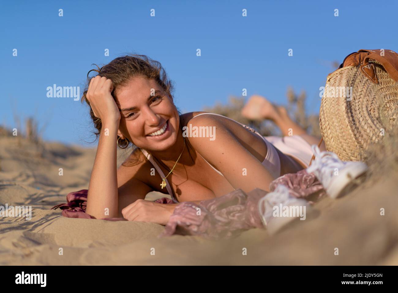 Happy young woman lying down enjoys her vacation in the sand by the beach. Stock Photo