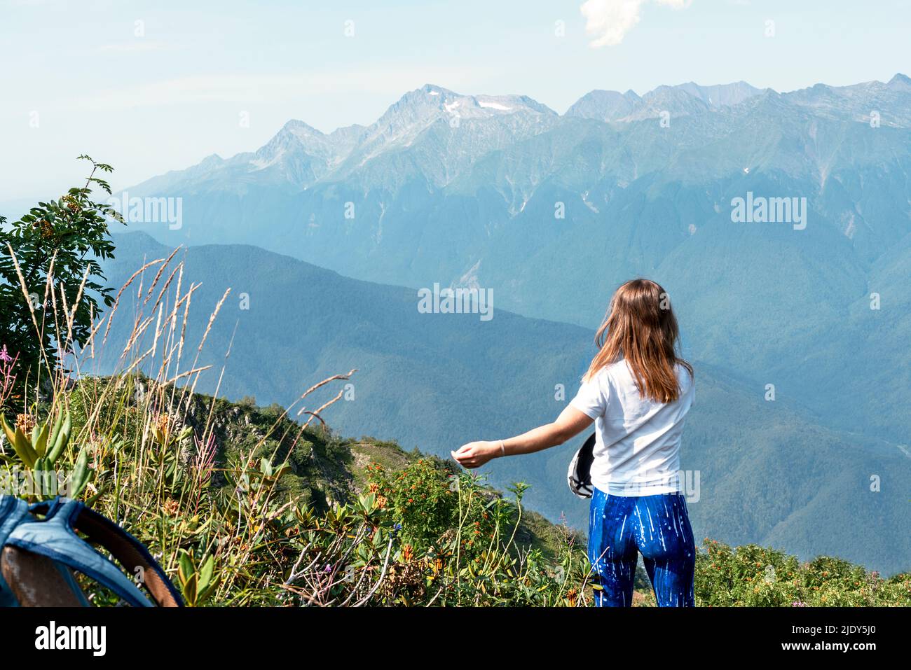 Happy young blonde woman rejoicing at view of the mountain range in the summer hike Stock Photo