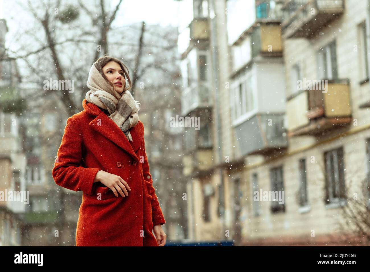 Beautiful brunette in a red coat on a city street under the snow. Stock Photo