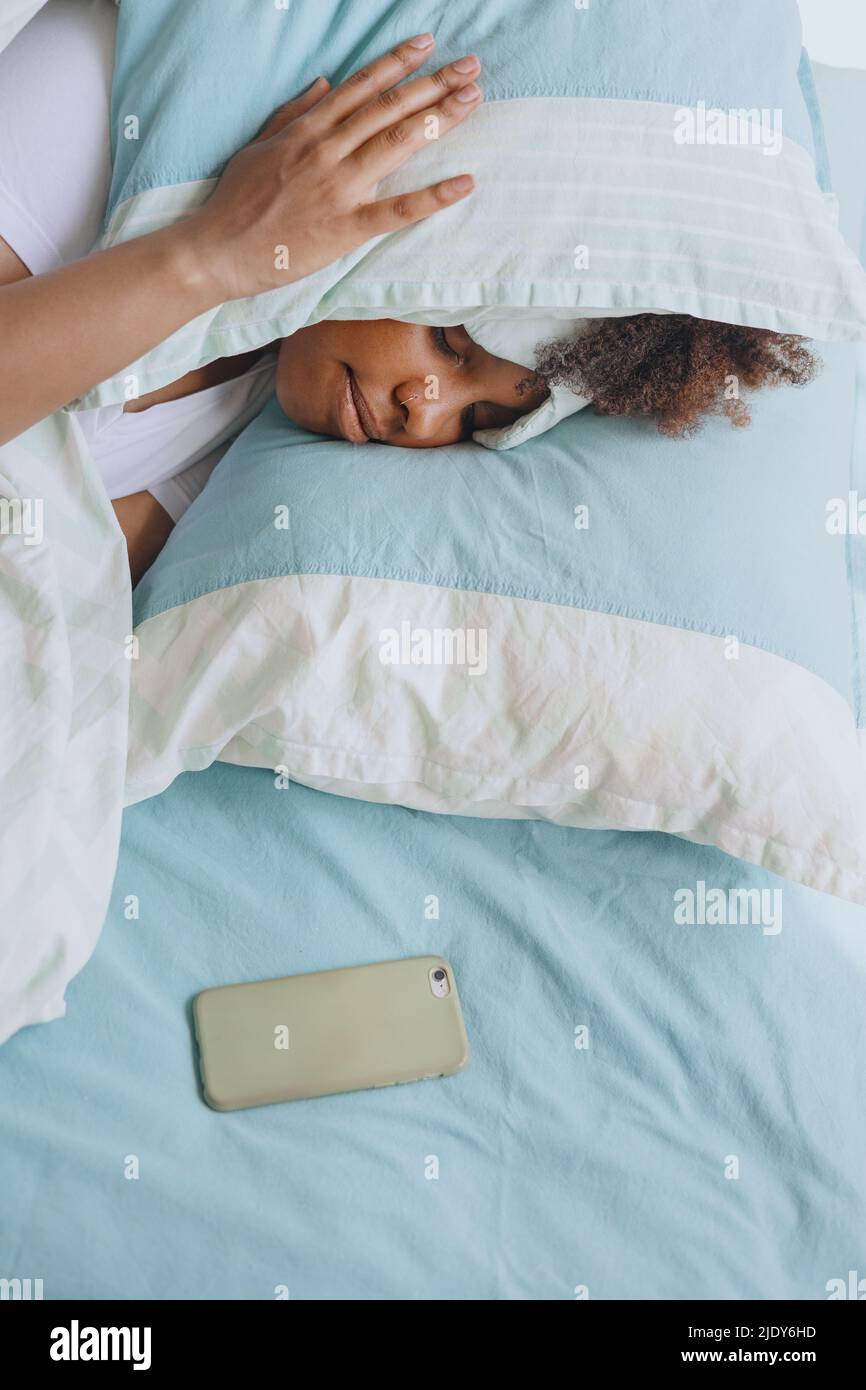 Woman sleeping with a pillow on her head and a phone nearby Stock Photo