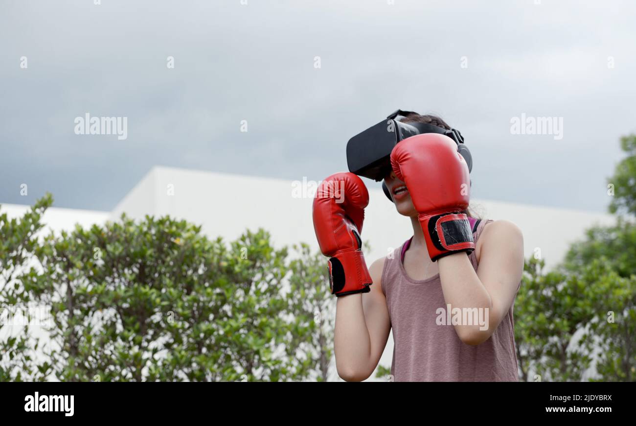 Young female wearing VR headset for working out boxing, aerobic training for boxing punch in virtual reality in simulation world. Stock Photo