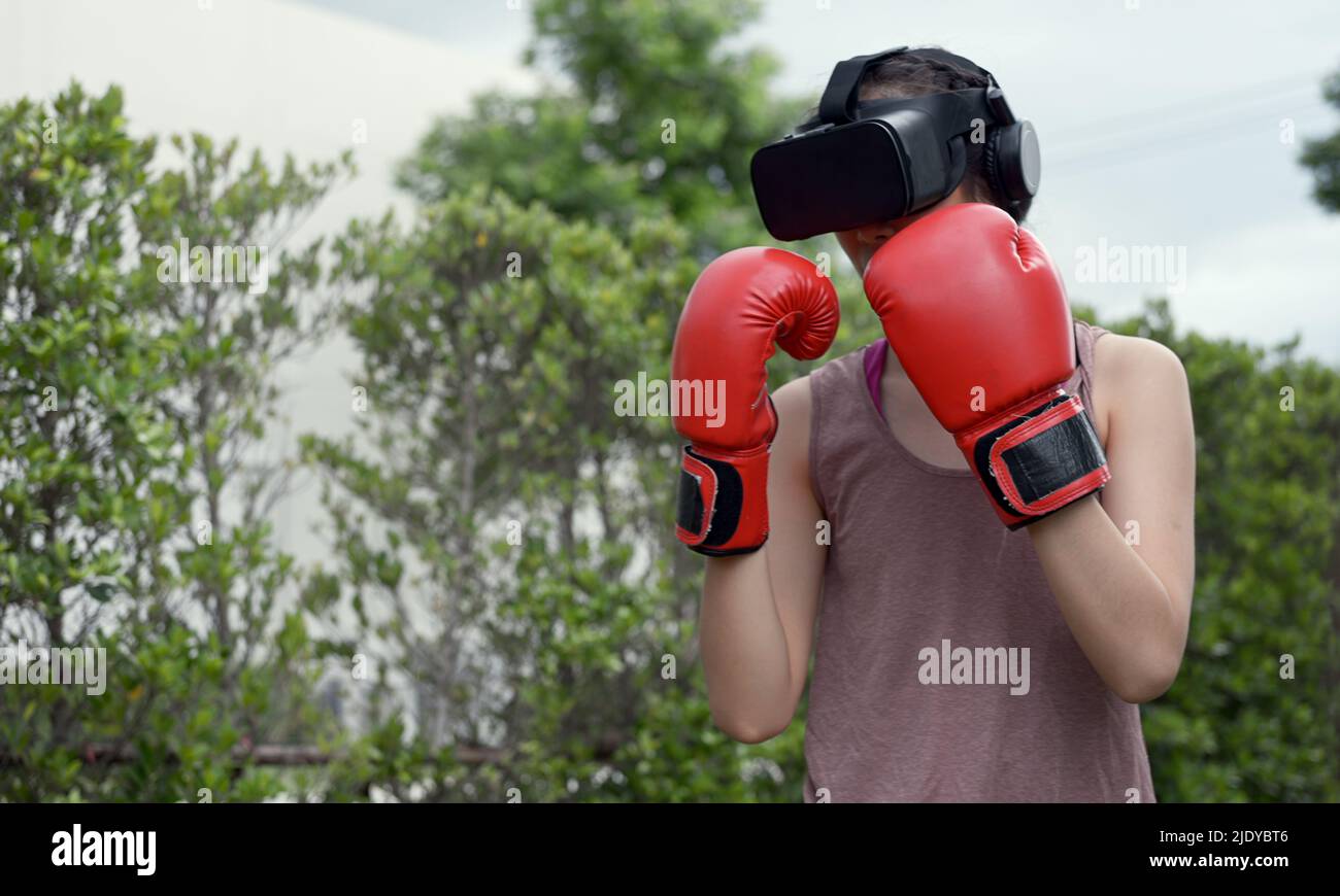 Young female wearing VR headset for working out boxing, aerobic training for boxing punch in virtual reality in simulation world. Stock Photo