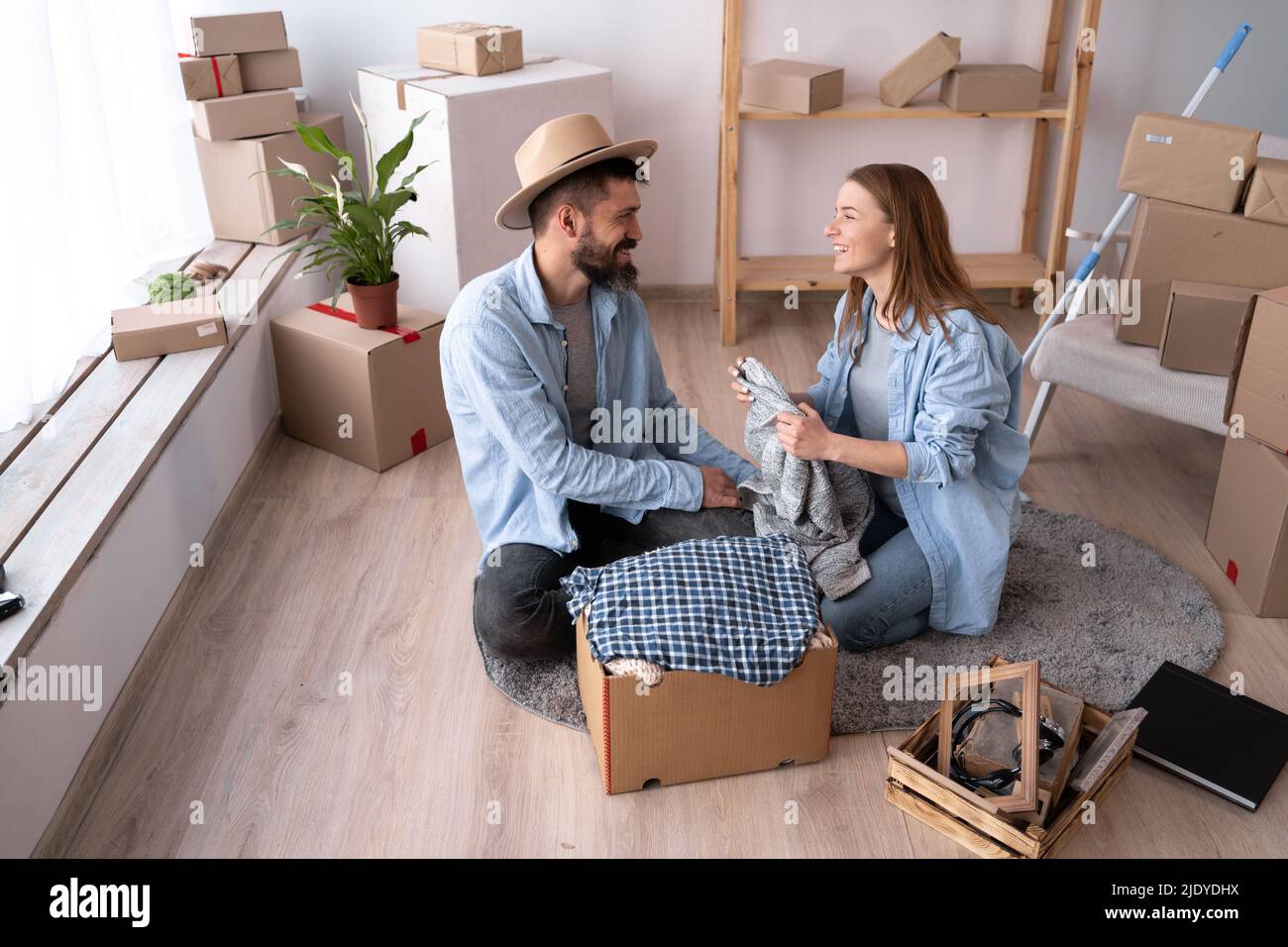 A man and a woman on the day of the move sit on the floor and unpack things. Happy couple in a new apartment. The concept of renting and buying a home Stock Photo
