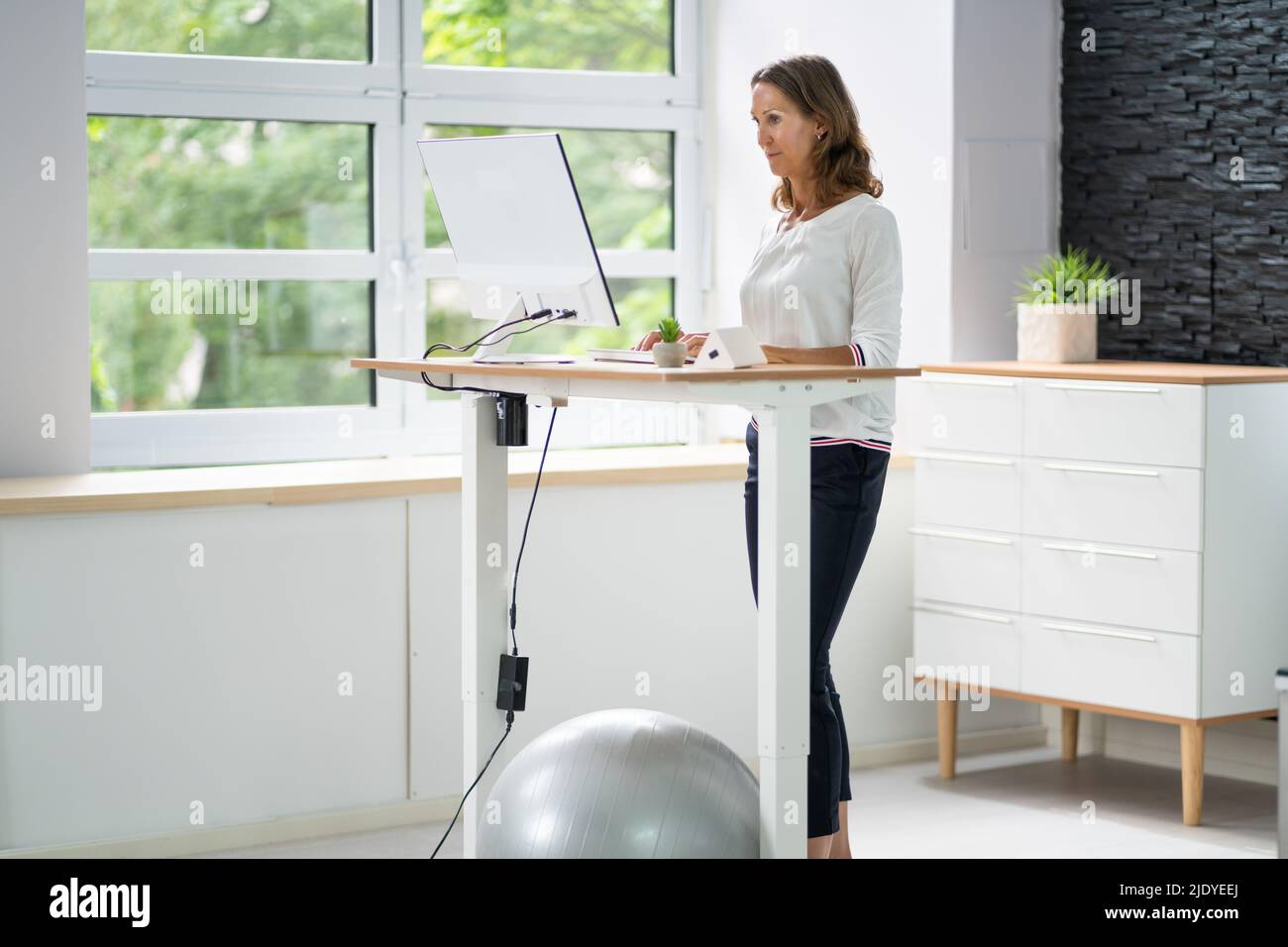 Woman Using Adjustable Height Standing Desk In Office For Good Posture