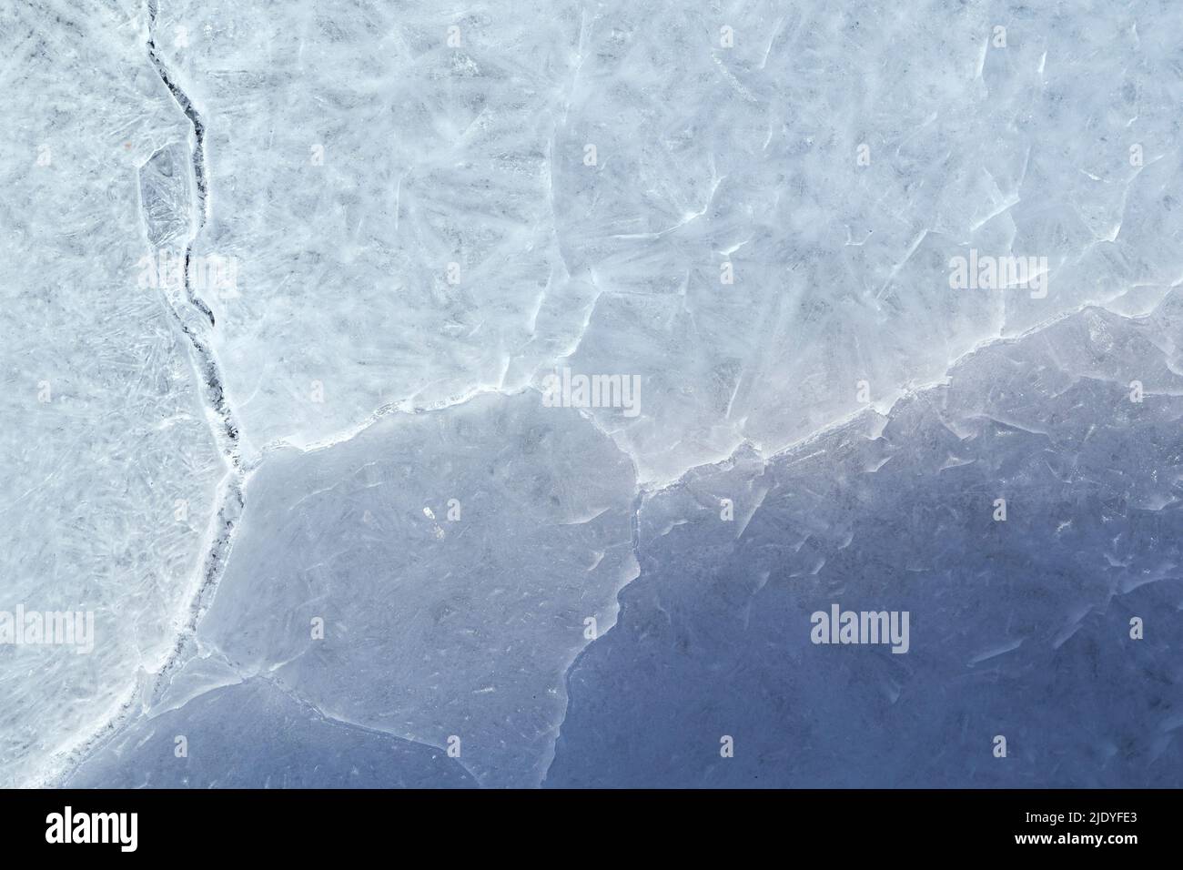Close-up of cracked ice on a frozen lake in the winter, viewed from above. Abstract textured full frame background. Copy space, top view. Stock Photo