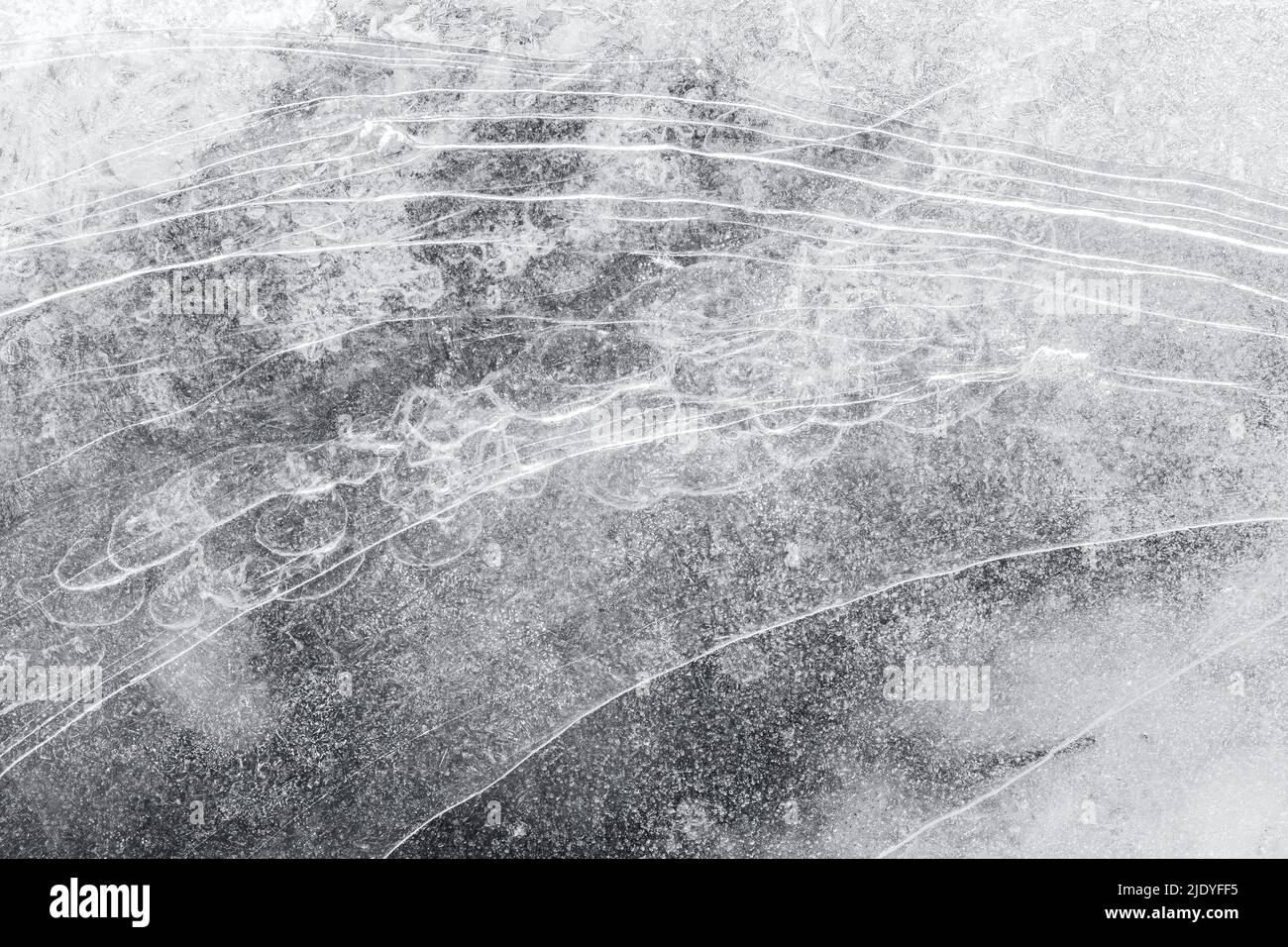 Macro close-up of ice on a frozen lake in the winter, viewed from above. Abstract full frame textured background in black&white. Copy space, top view. Stock Photo