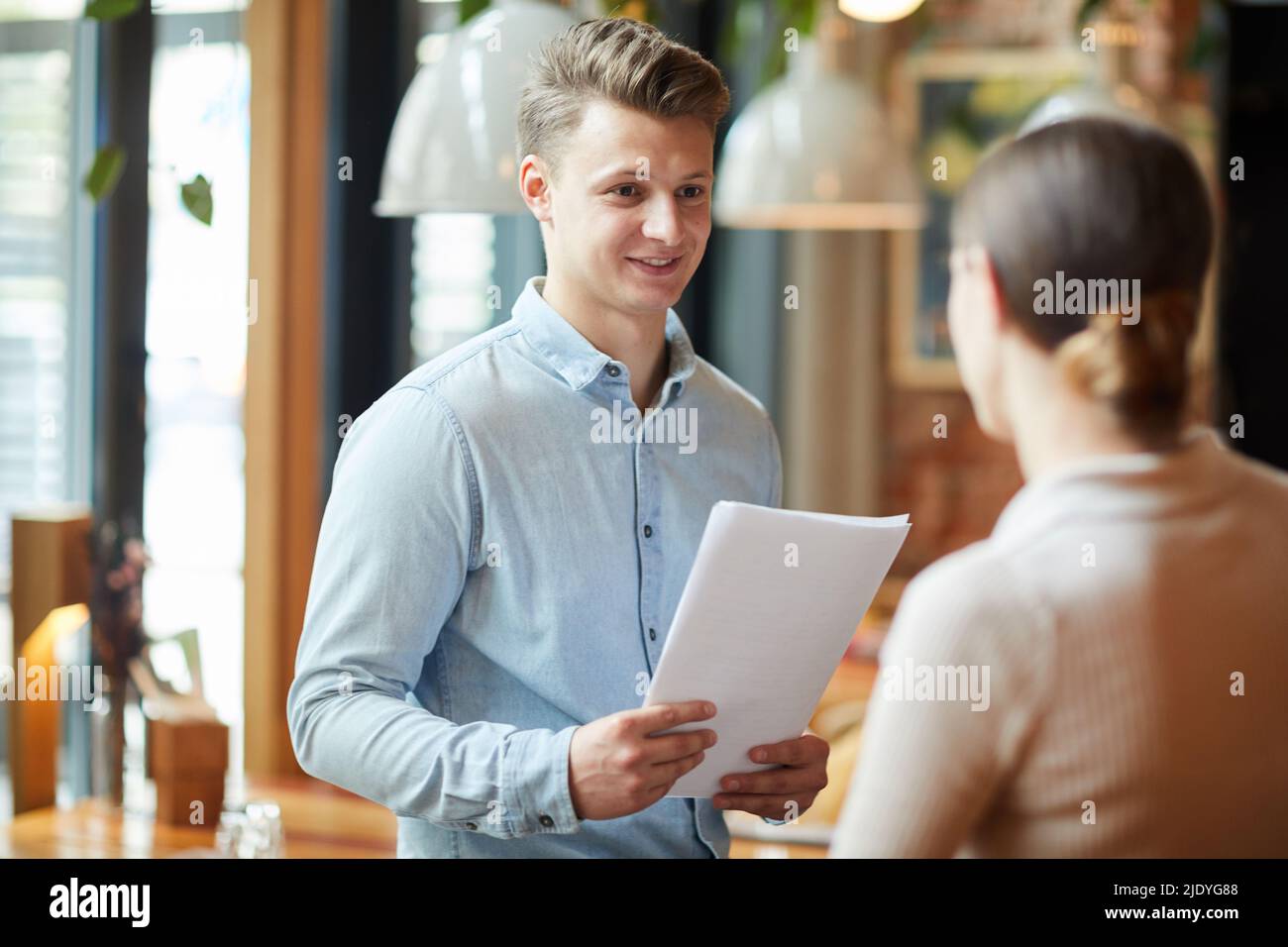 Content young male restaurant manager with papers standing in cafe and talking to waitress about customer service Stock Photo