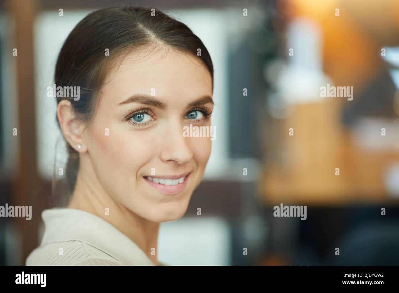 Portrait of positive confident girl with blue eyes smiling at camera while standing in modern cafe Stock Photo