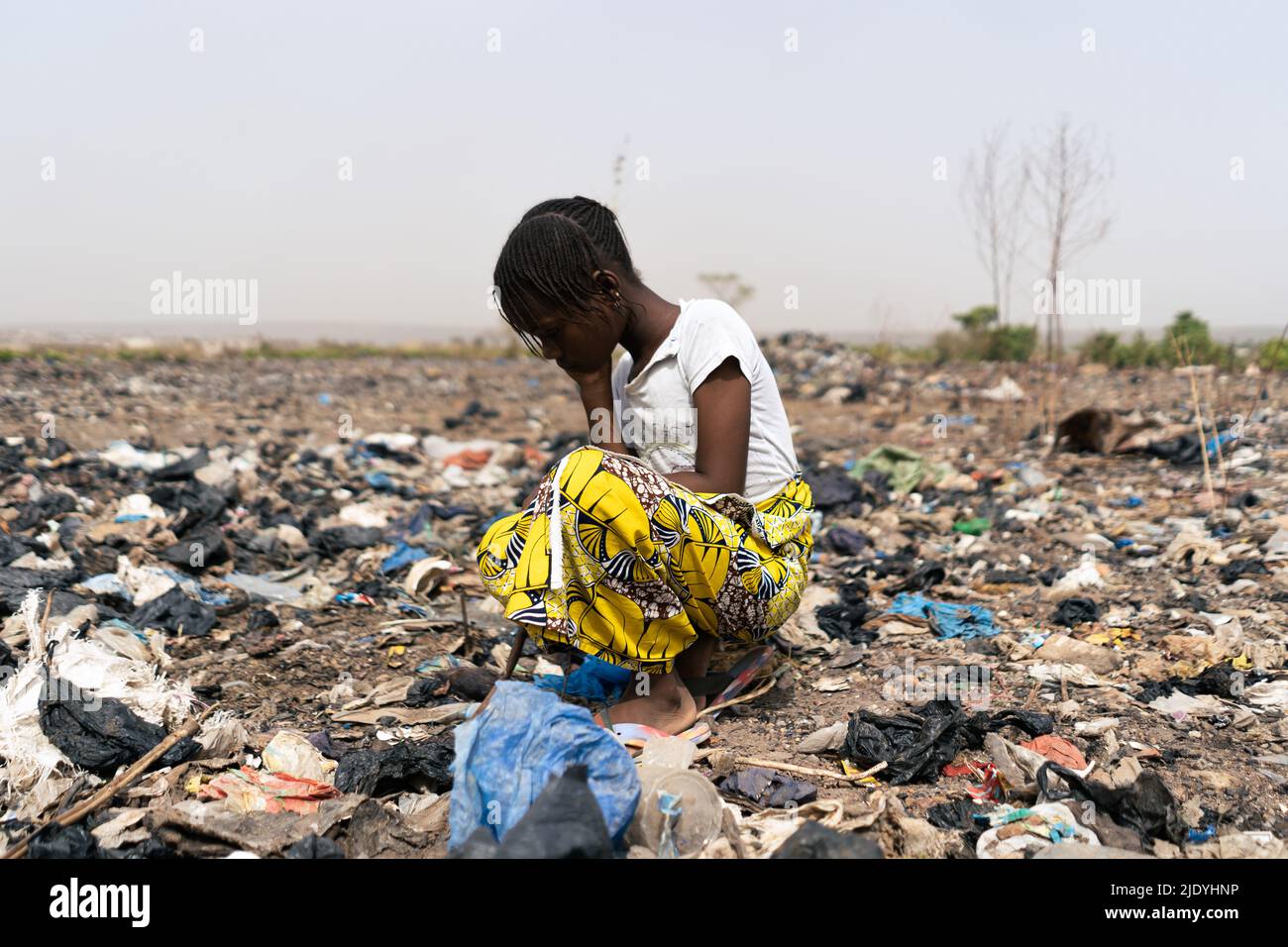 Tired little African girl who is desperately looking in the rubbish heap for objects that can be used; extreme poverty and hopelessness of the black c Stock Photo