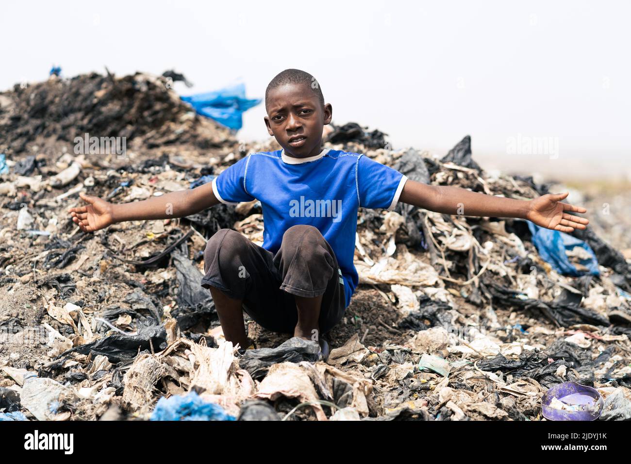 Young black African boy inviting the viewer to contemplate the chaos of garbage, decay and filth around him; symbol of the legacy of previous generati Stock Photo