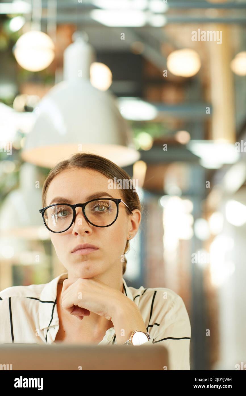 Portrait of serious confident attractive young lady in stylish spectacles using modern laptop in cafe Stock Photo