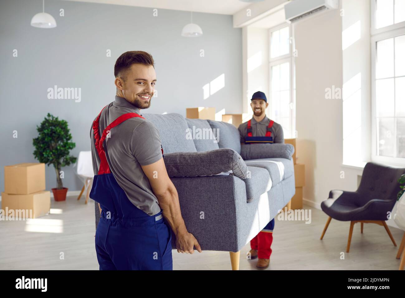 Male workers of furniture delivery service move sofa to customer's new