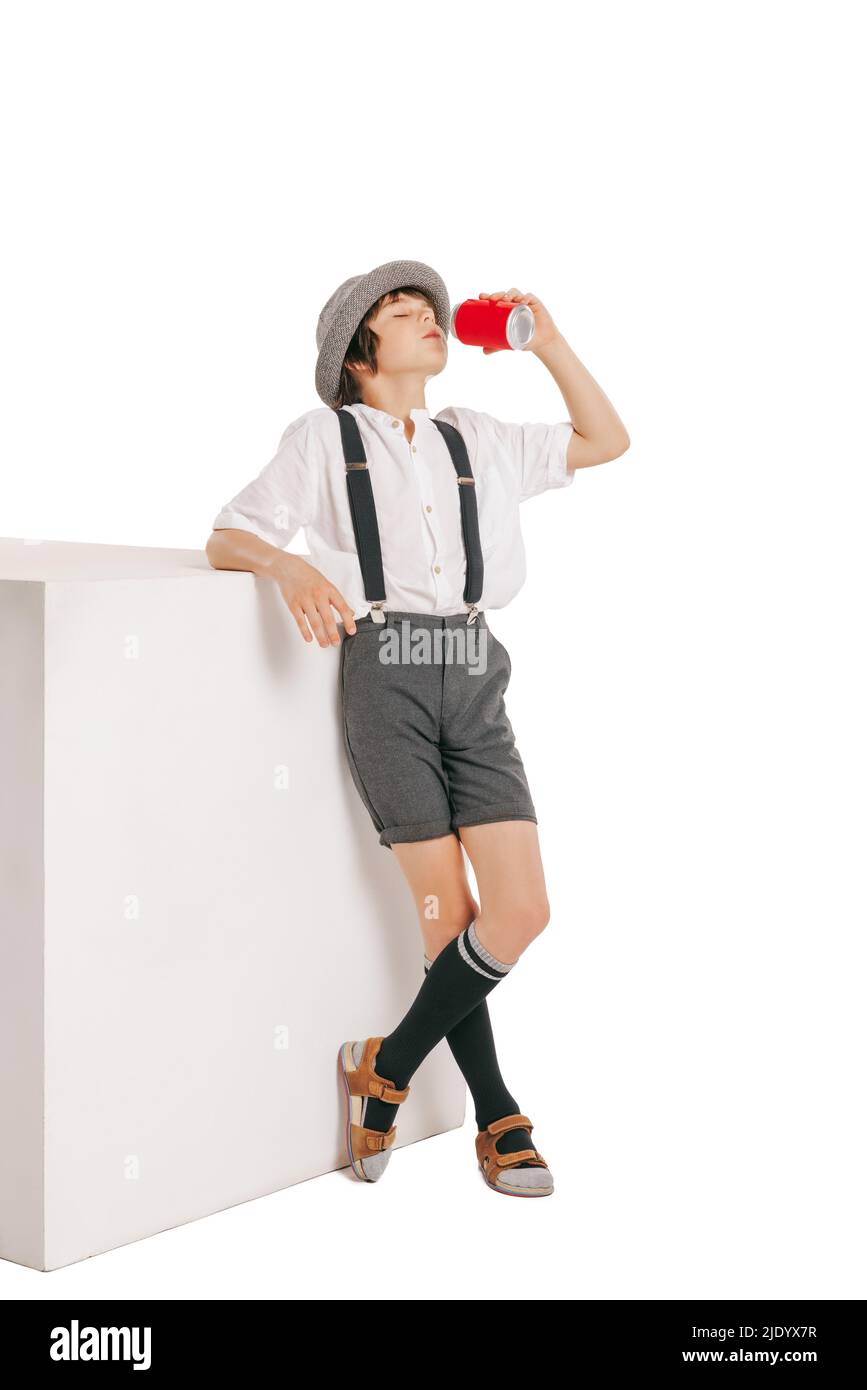 Stylish boy, kid wearing hat and shorts with suspenders drinking