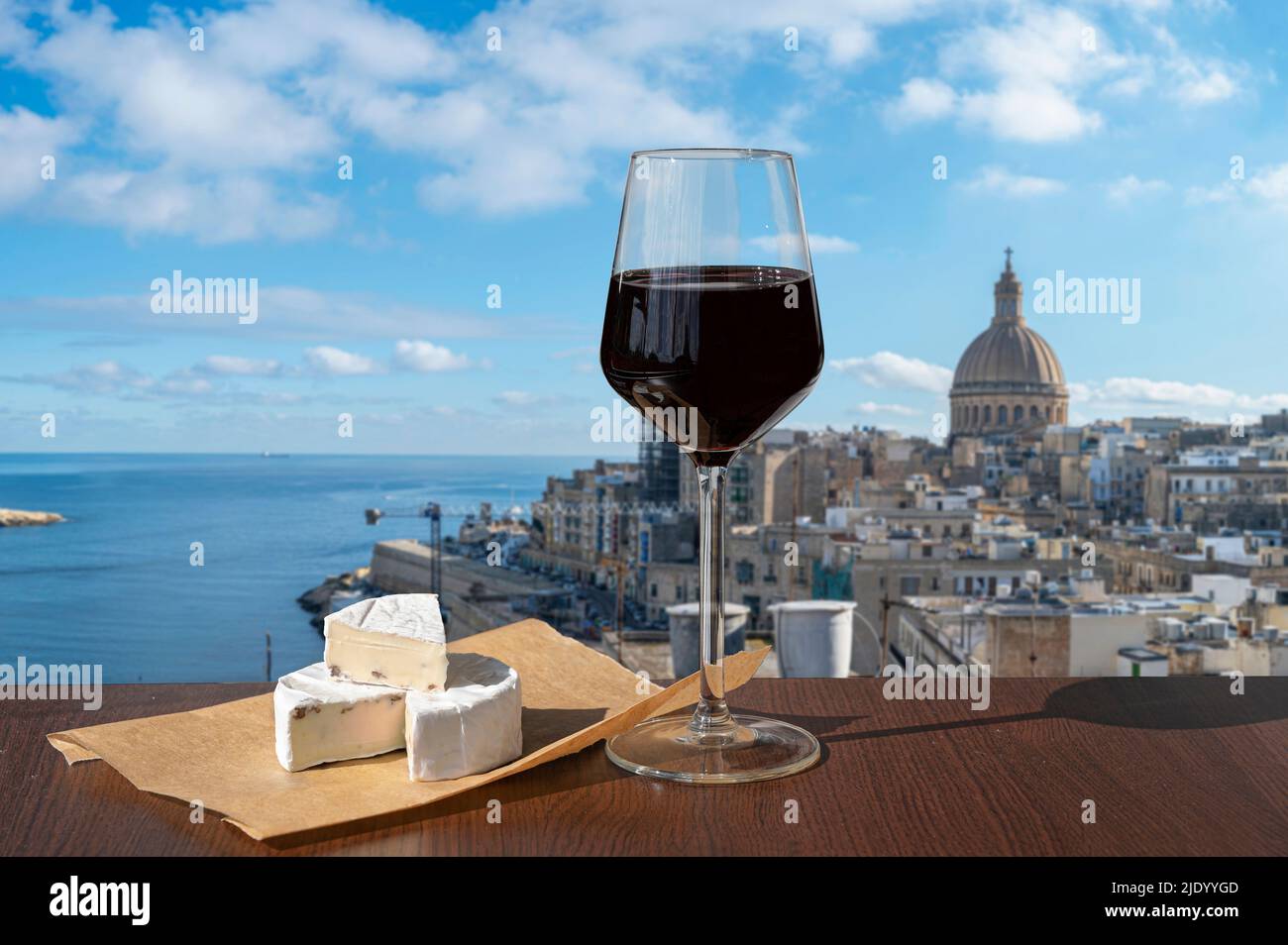 Glass of red wine with cheese with view of Valletta old town and harbor in Valletta, Malta. Stock Photo