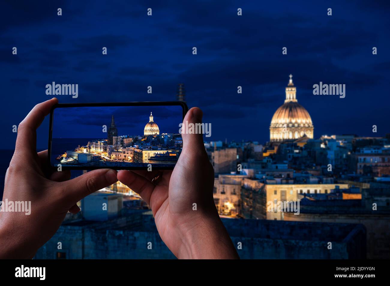 Tourist taking photo of illuminated at night Valletta old town and harbor in Valletta, Malta. Stock Photo