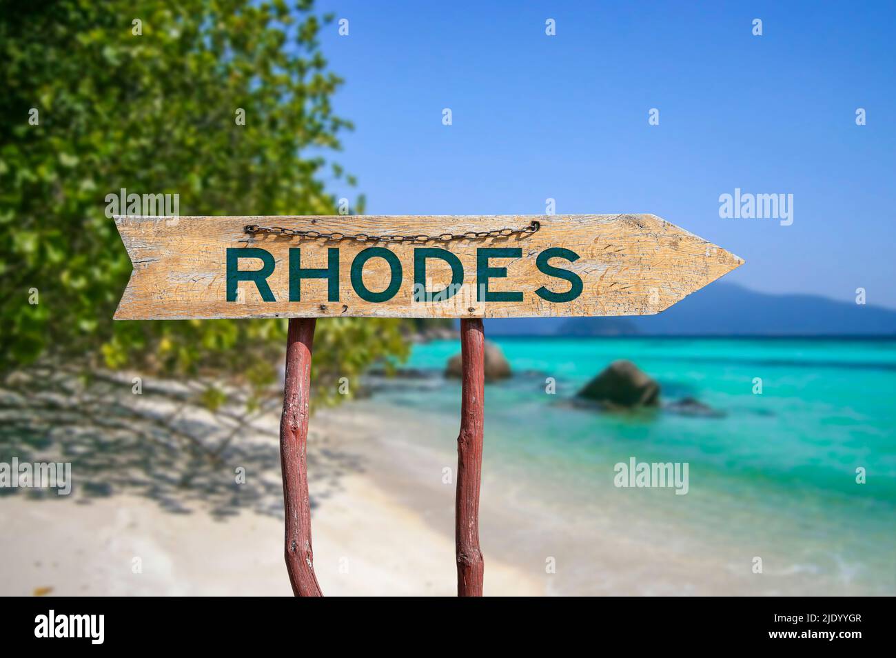 Rhodes wooden arrow road sign against beach with white sand and turquoise water background. Travel to Greece concept. Stock Photo