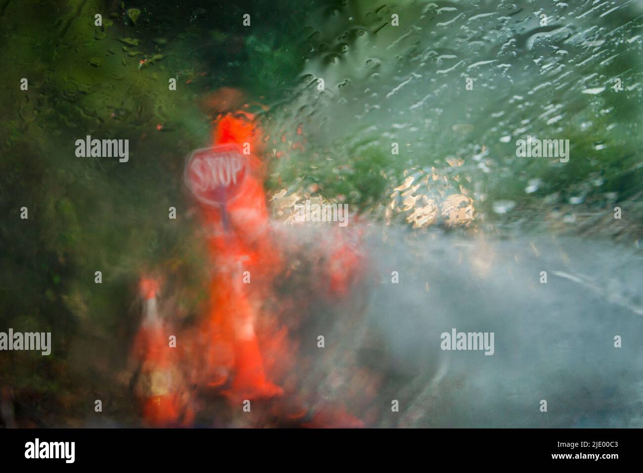 Worker wearing high visibility orange clothing with Stop sign in the heavy rain. Photo taken using intentional camera movement behind rain spattered c Stock Photo
