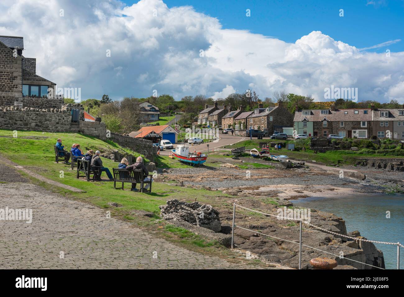 Craster Northumberland, view in summer of people sitting on benches enjoying the view of the scenic harbour in Craster on the Northumberland coast, UK Stock Photo