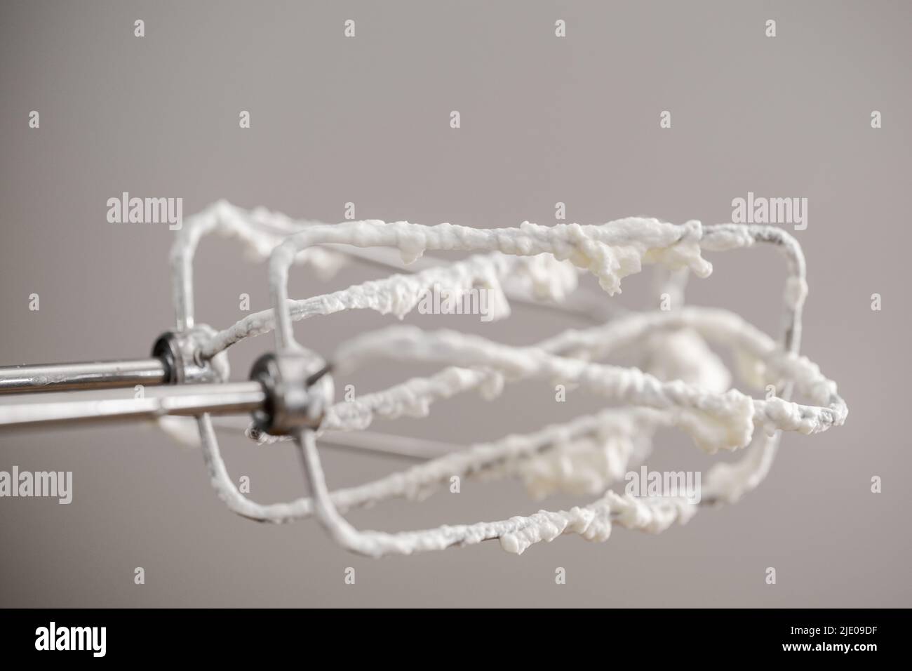 Detail of stirring gear of kitchen mixer with whipped cream on neutral grey background Stock Photo
