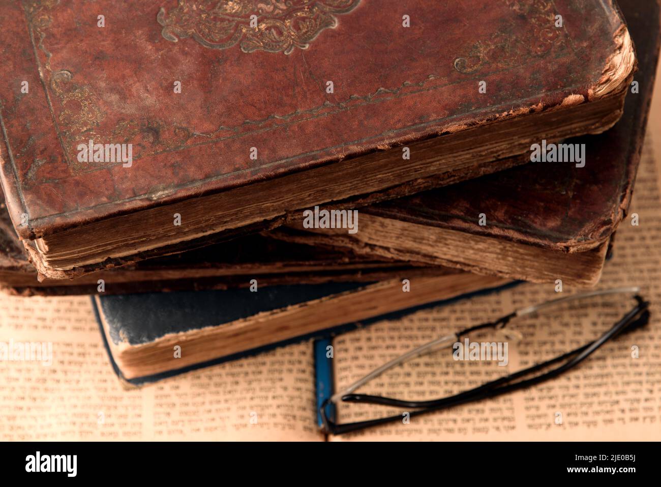 Old worn shabby leather-bound jewish books on open blurred Torah in the background. Closeup. Selective focus Stock Photo