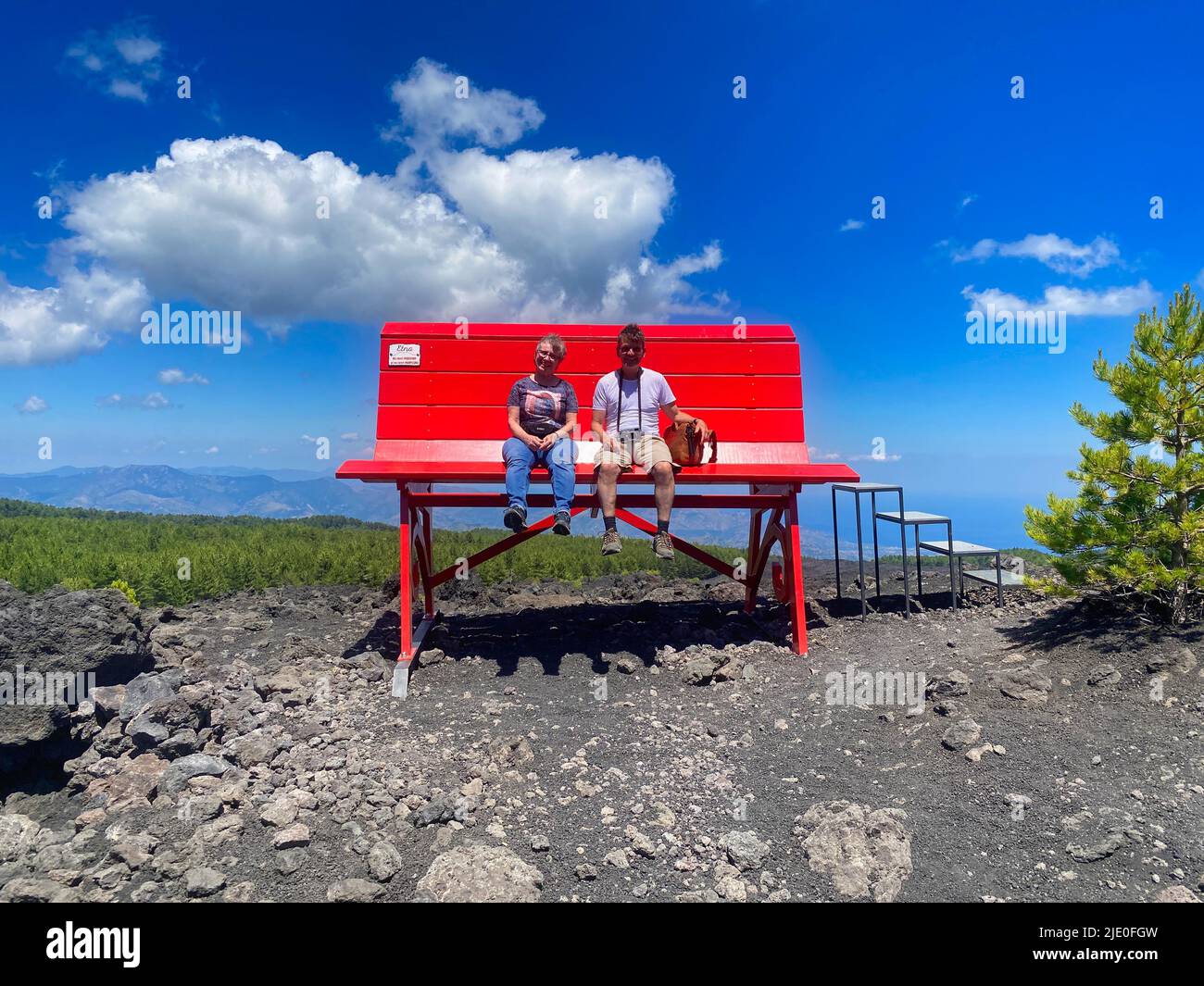 2 people sitting on huge red bench, Big Bench Community Project, Big Bench Number 200, Etna, Grande Panchina, Linguaglossa, Sicily, Italy Stock Photo