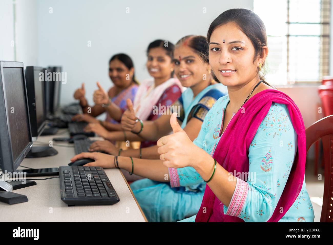 group of smiling women showing thumbs up by looking camera during computer training class - concept of women employment, learning and education Stock Photo