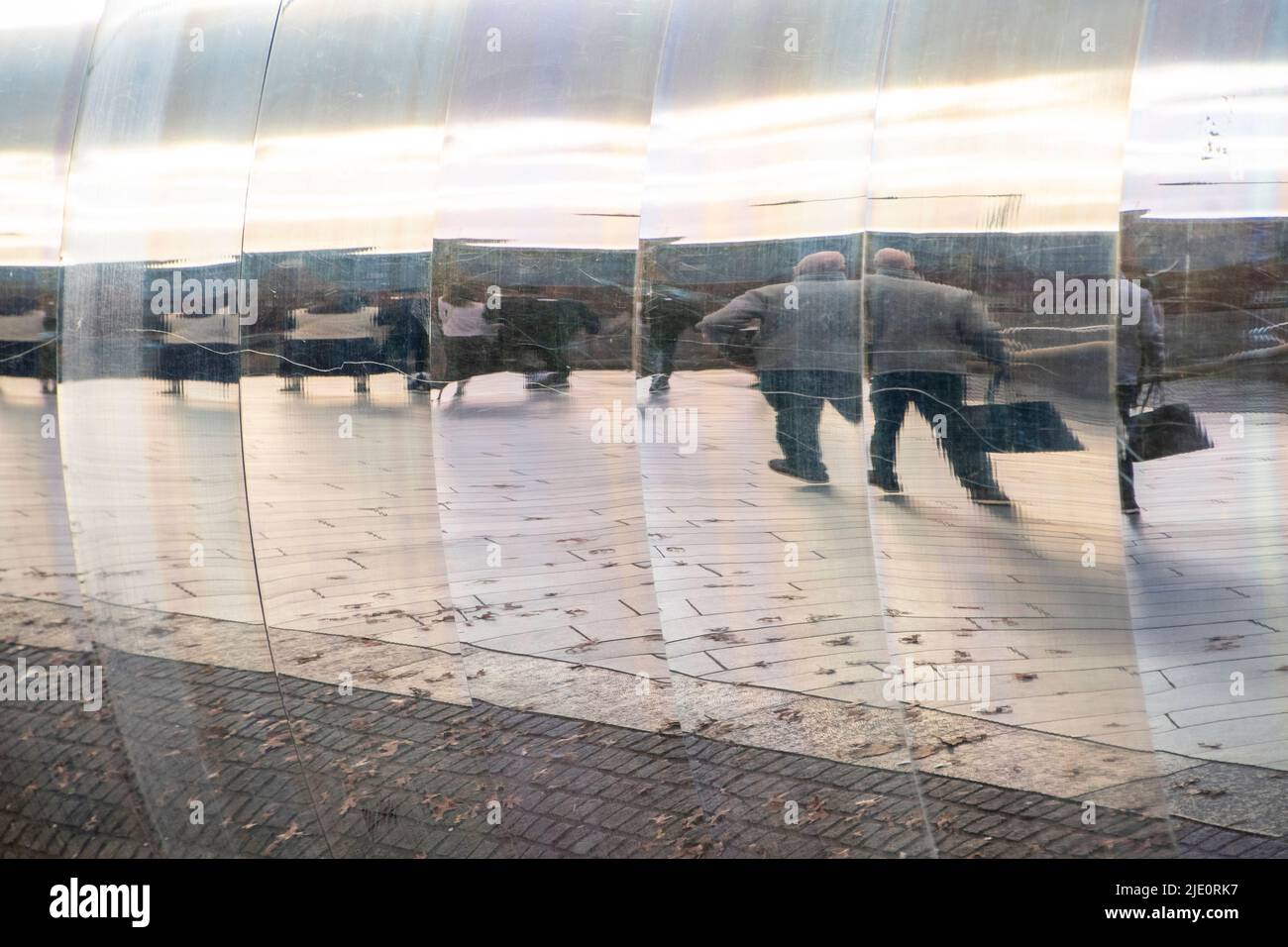 Sheffield, UK – 13 November 2021: Passersby walking towards the train station reflected in the curved metal wall of The Cutting Edge sculpture, Sheaf Stock Photo