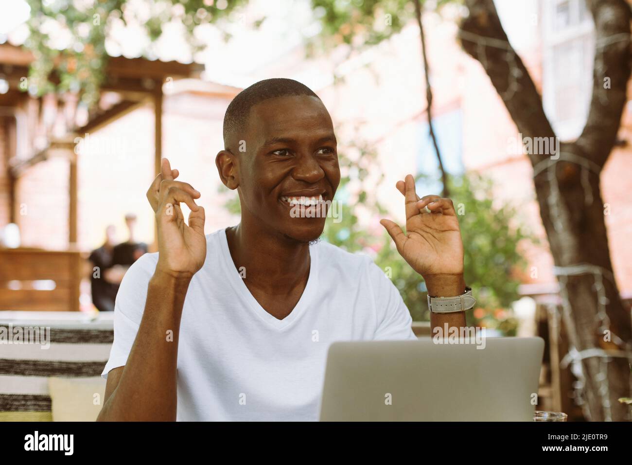 Smiling african american businessman work on laptop in the cafe, crossing fingers, wish good luck. Conclusion contract Stock Photo