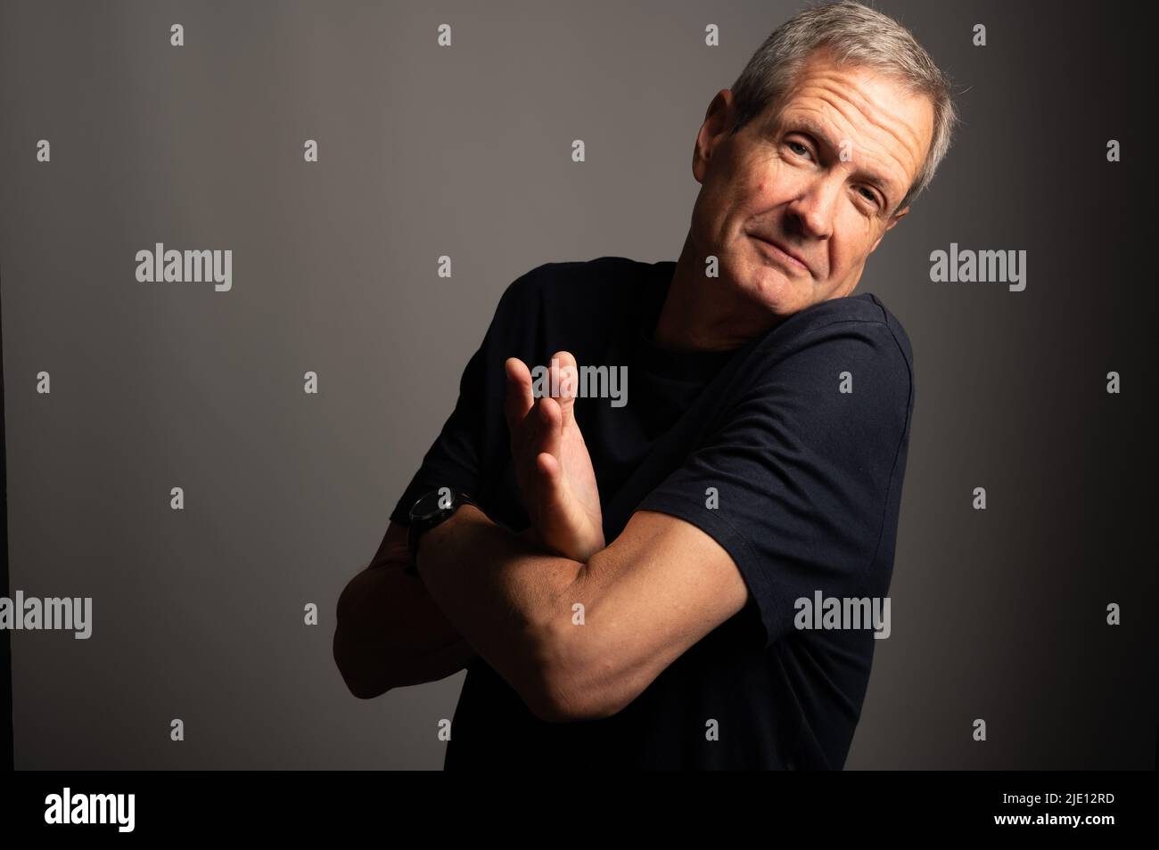 Mature man shrugging, on a grey background with copy space Stock Photo