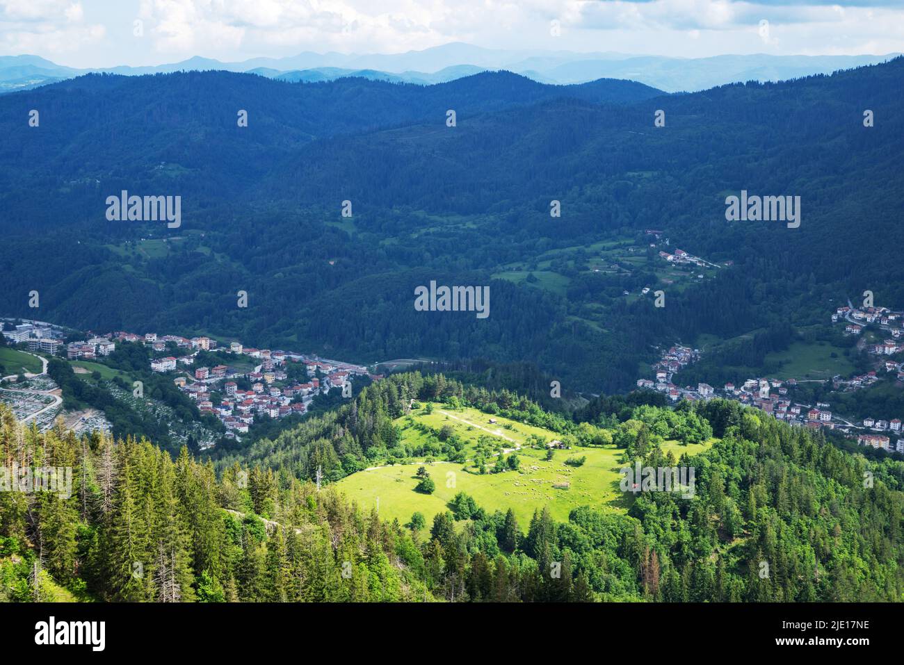 Green spring mountain valley sheltered by mountain vegetation and spruce dark dense forests with small old cattle village of Smolyan, with bright gras Stock Photo