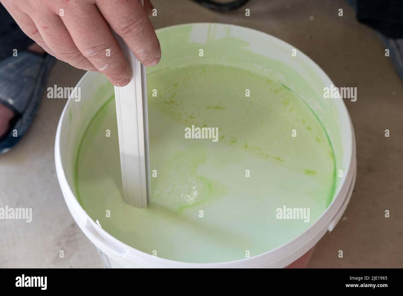 Worker's hands stir green paint before applying it, closeup. Bucket