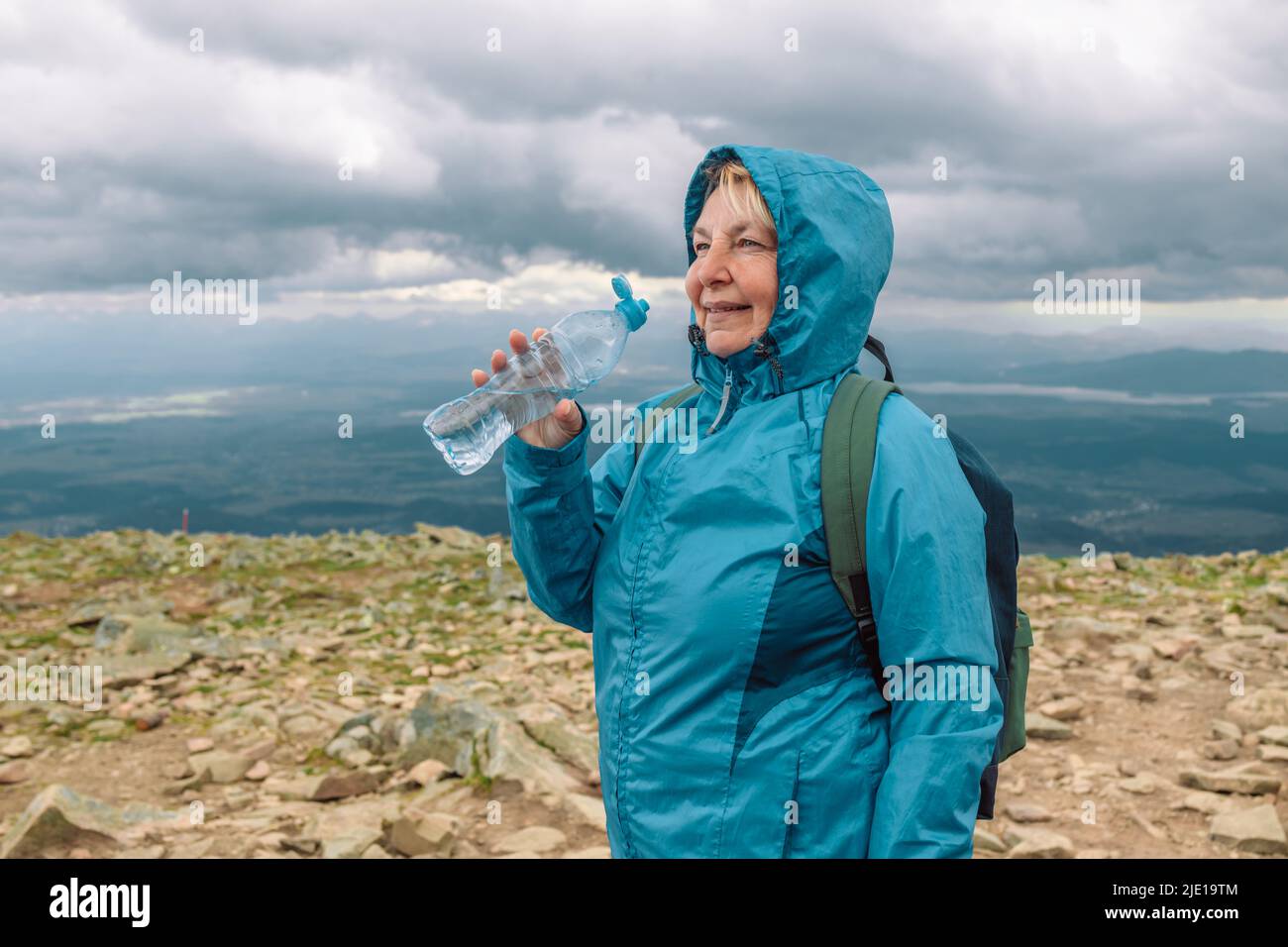 Tired female 50s hiker drinking water from the bottle with backpack