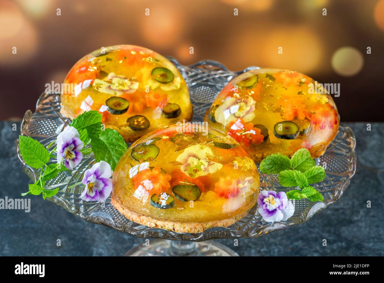 Lemon jelly globes with fresh fruit, edible flowers and gold flakes on pistachio biscuit - gourmet dessert Stock Photo