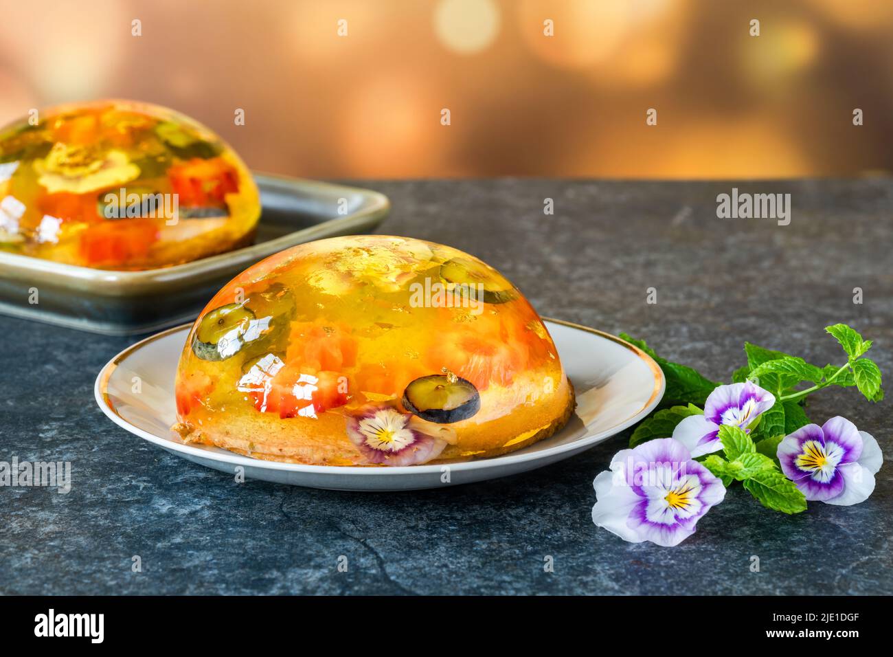 Lemon jelly globes with fresh fruit, edible flowers and gold flakes on pistachio biscuit - gourmet dessert Stock Photo