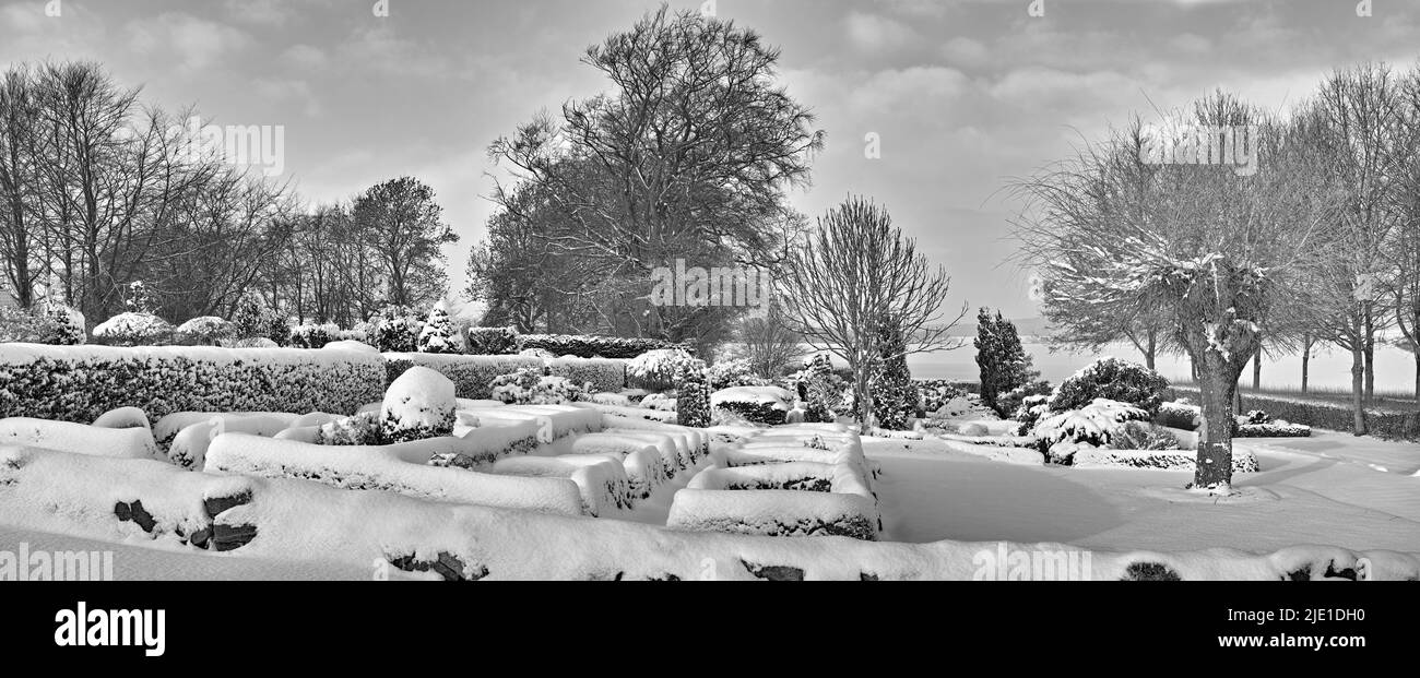 Gloomy graveyard in a monochrome winter landscape. Snow covered gravestones against a grey cloudy sky. Black and white empty frosted cemetery and Stock Photo